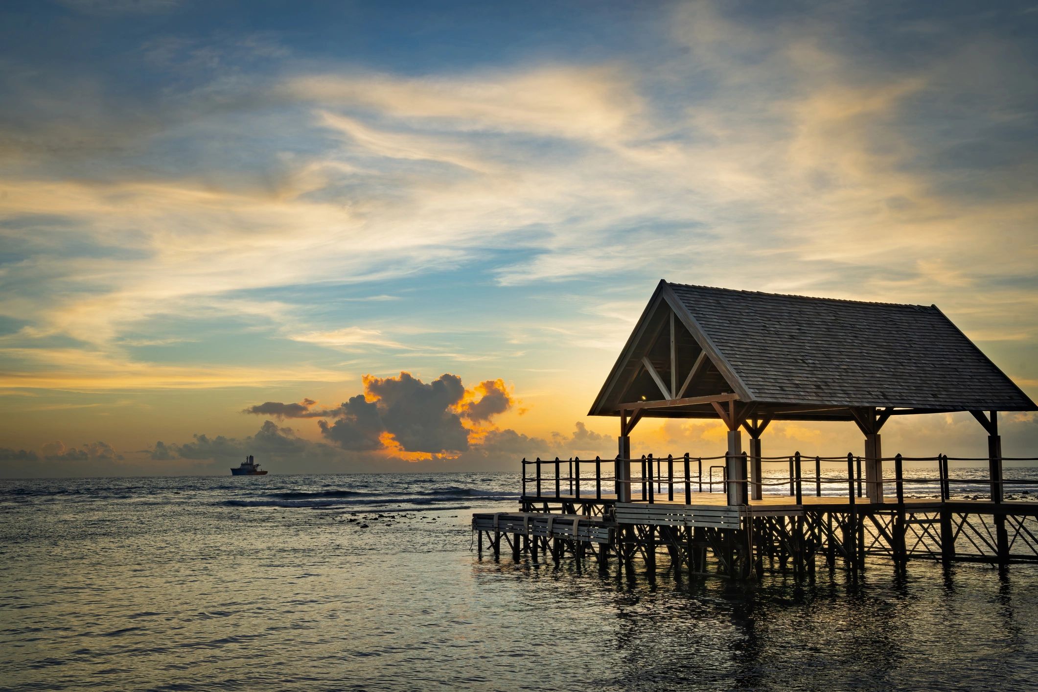 Wooden pier and pavilion at sunset over calm tropical ocean